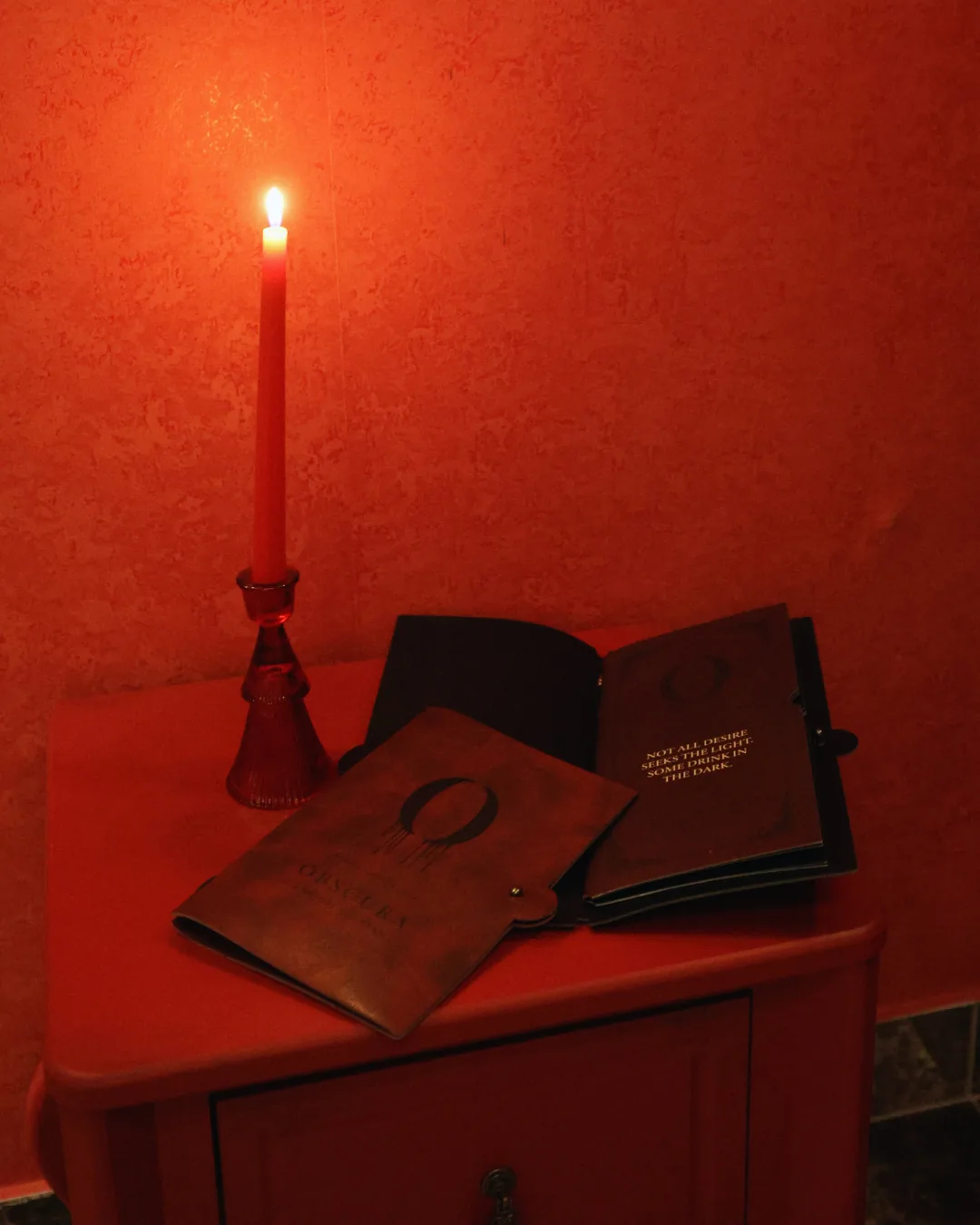Obscura cocktail menus by candlelight on a red table